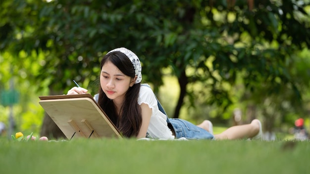 Charmante fille femme assise sur un plaid au parc en journée d'été ensoleillée et à l'aide d'aquarelle