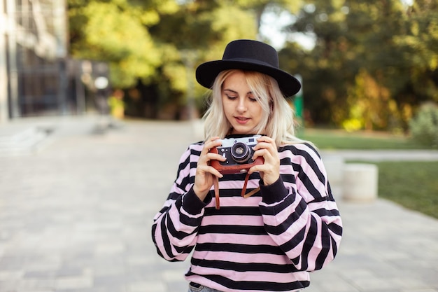 Charmante fille hipster avec un chapeau et une caméra rétro à l'extérieur