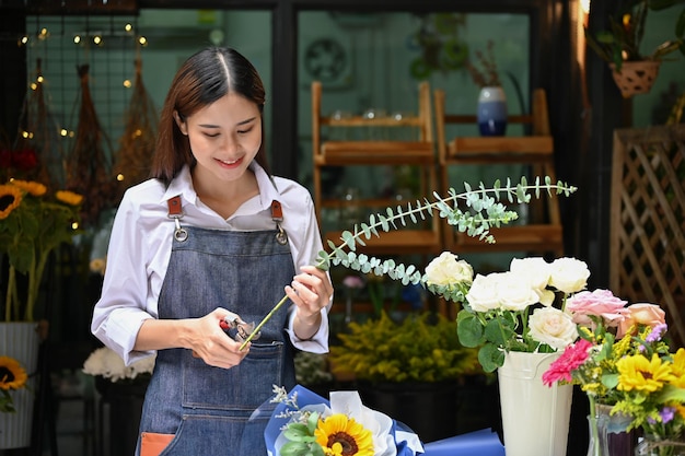 Charmante fleuriste asiatique faisant un beau bouquet coupant une tige de fleur