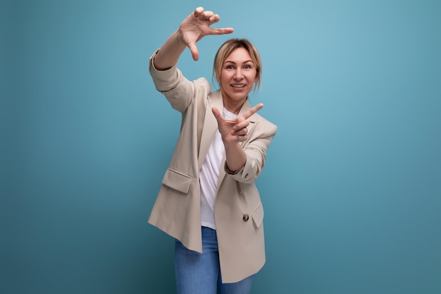 Charmante jeune femme d'affaires blonde dans une veste fait une photo avec ses mains sur un fond de studio