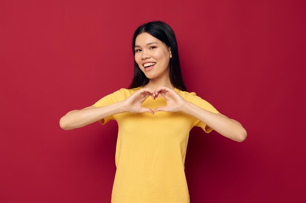 Charmante jeune femme asiatique jaune t-shirt décontracté sourire posant fond rouge inchangé