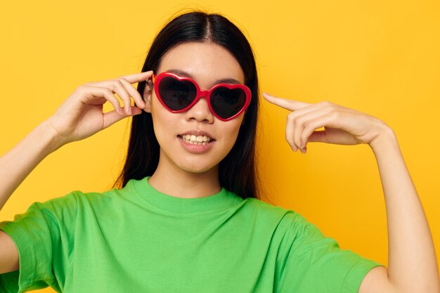 Charmante jeune femme asiatique à lunettes noires dans un t-shirt vert posant un fond jaune moderne inchangé