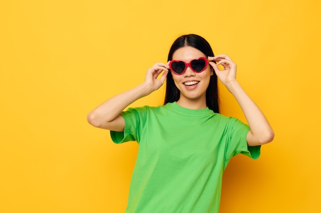 Charmante jeune femme asiatique à lunettes noires dans un t-shirt vert posant un fond jaune moderne inchangé