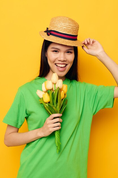 Charmante jeune femme asiatique tshirt vert un bouquet de fleurs jaunes dans un chapeau fond isolé inchangé