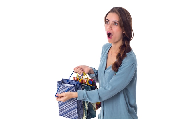 Charmante jeune femme en blouse bleue tenant des sacs à provisions multicolores et montrant l'étonnement