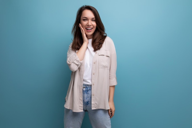 Charmante jeune femme brune en vêtements informels souriant sur fond bleu