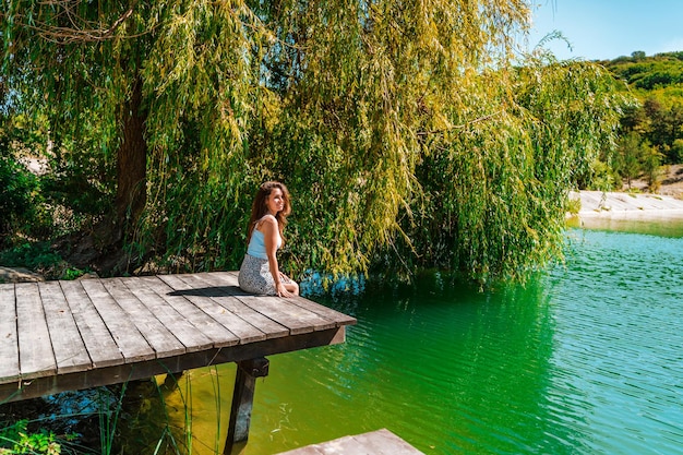 Une charmante jeune femme en jupe est assise sur un pont en bois sur fond de nature