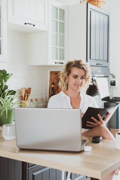 Charmante jeune femme avec ordinateur portable travaillant à la maison dans la cuisine