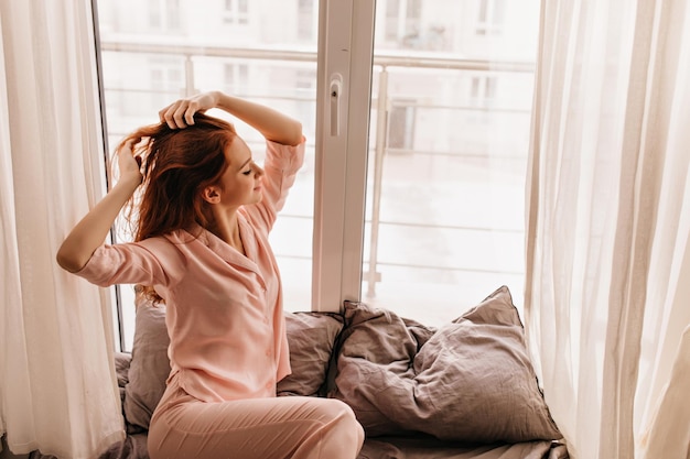 Charmante jeune femme en pyjama posant à côté de la fenêtre