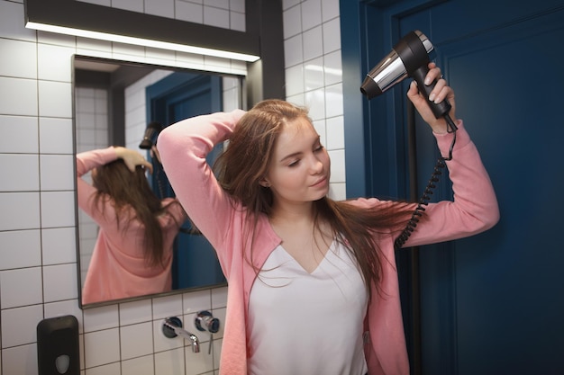 Charmante jeune femme séchant ses cheveux dans la salle de bain