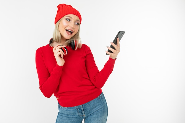 Charmante jeune femme souriante dans des vêtements rouges avec un casque et un téléphone sur un fond de studio blanc