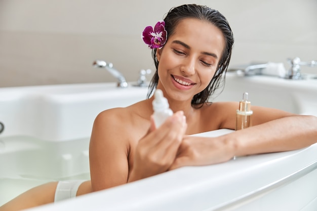 Charmante jeune femme tenant un sérum vitaminé tout en prenant un bain