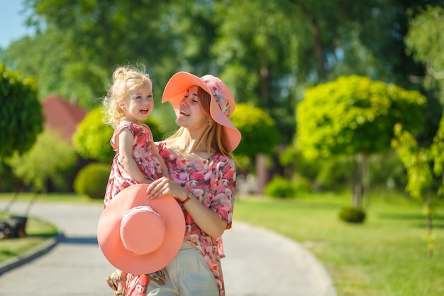 Une charmante jeune fille dans une robe d'été légère se promène dans un parc verdoyant avec sa petite fille, la tenant dans ses bras. Bénéficie des chaudes journées d'été ensoleillées.