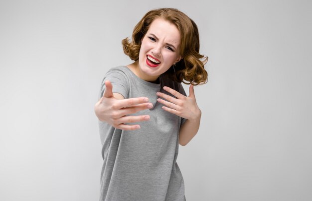 Charmante jeune fille dans un t-shirt gris sur fond gris. La fille tendit les bras en avant