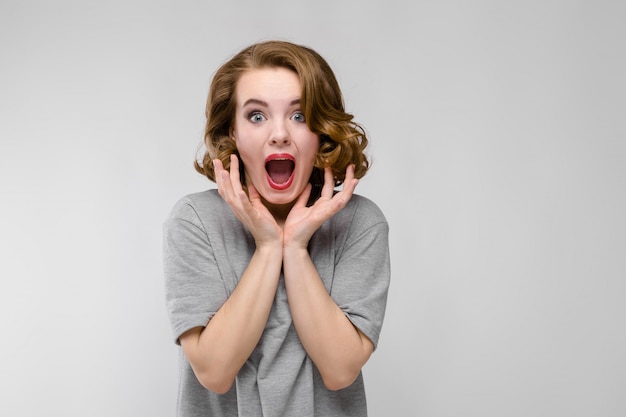 Charmante jeune fille dans un t-shirt gris sur un gris. La fille crie de bonheur