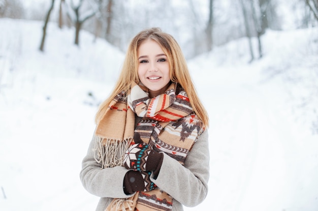 Charmante jeune fille douce dans un manteau élégant d'hiver dans une écharpe en laine vintage dans des mitaines chaudes et élégantes