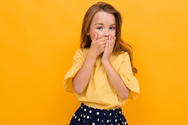 Charmante jeune fille élégante dans un chemisier jaune clair et une jupe sombre couvrait sa bouche avec ses mains sur un fond jaune