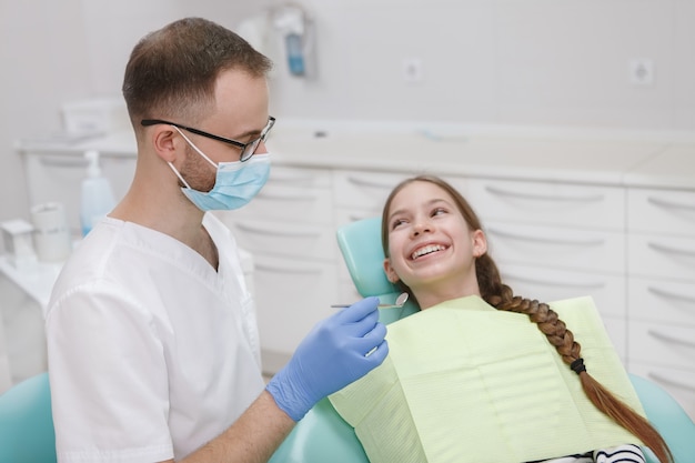 Charmante jeune fille souriante à son dentiste lors de l'examen dentaire