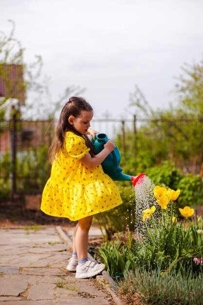 Une charmante jeune fille vêtue d'une robe jaune flottant au vent arrose des tulipes jaunes d'un arrosoir dans...