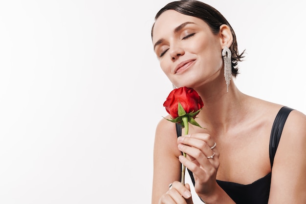 charmante jeune jolie femme glamour souriante et tenant une fleur isolée sur un mur blanc