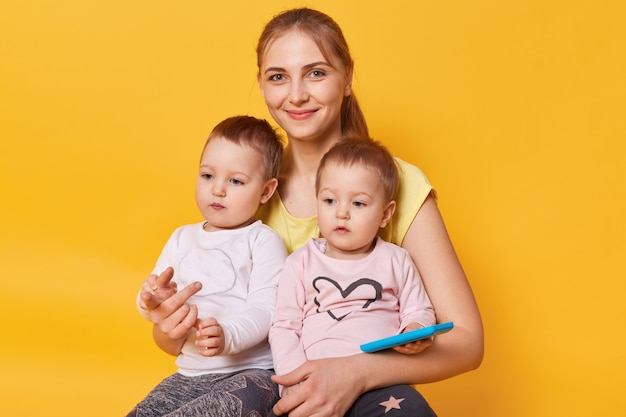 Charmante maman affectueuse assise avec ses mignonnes petites filles sur le sol en studio jaune