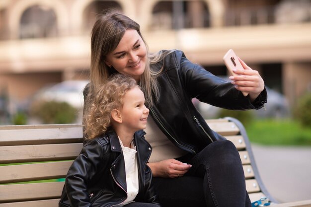 La charmante maman tient le téléphone et prend un selfie avec sa fille, la fille rit