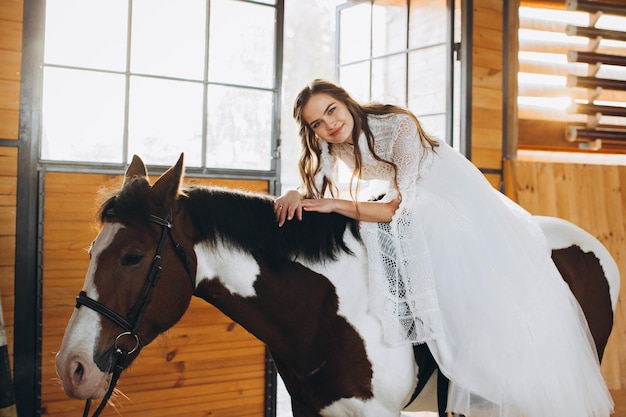 Une charmante mariée bohème monte à cheval dans un ranch au coucher du soleil en hiver