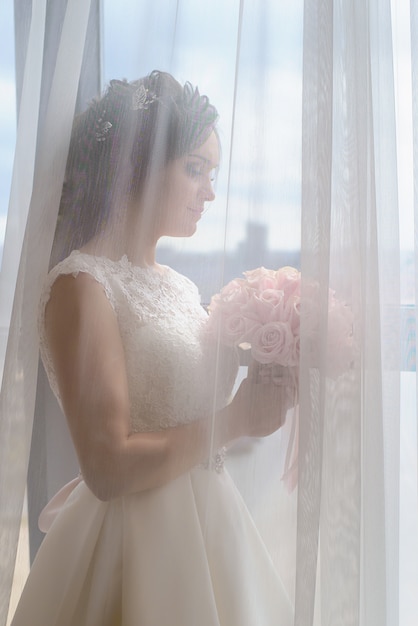 Charmante mariée à la fenêtre avec un bouquet de mariée
