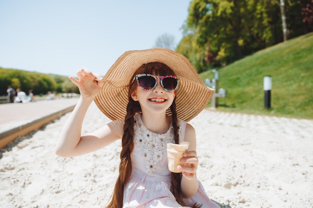 Charmante petite fille au chapeau mange de la glace sur la plage de la plage Concept de vacances d'été