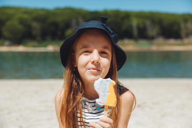 Charmante petite fille au chapeau mange de la glace sur la plage de la plage Concept de vacances d'été