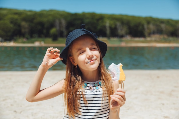 Charmante petite fille au chapeau mange de la glace sur la plage de la plage Concept de vacances d'été