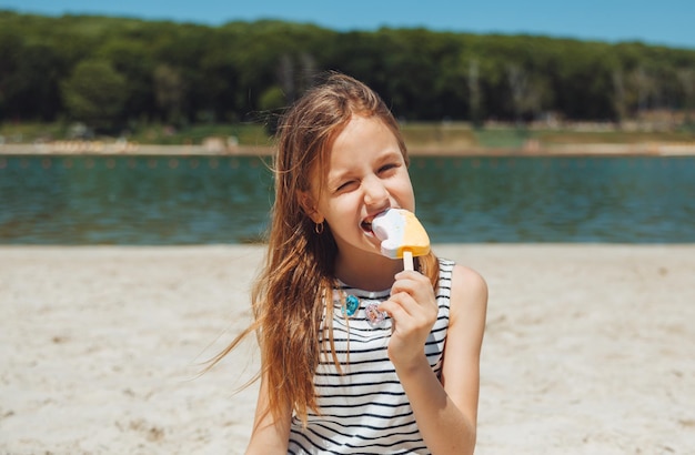 Charmante petite fille au chapeau mange de la glace sur la plage de la plage Concept de vacances d'été