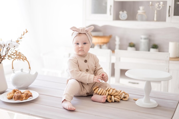 Une charmante petite fille dans une combinaison en tissu naturel est assise sur la table à la maison dans une cuisine lumineuse le premier leurre