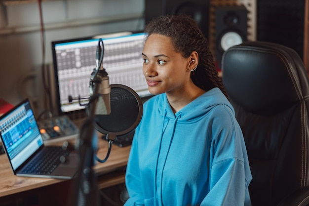 Photo charmante présentatrice de radio ethnique avec des dreadlocks élégants travaillant dans un studio d'enregistrement audio de diffusion