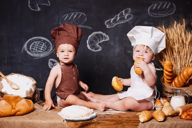 Charmants petits bambins en tablier sur table avec du pain