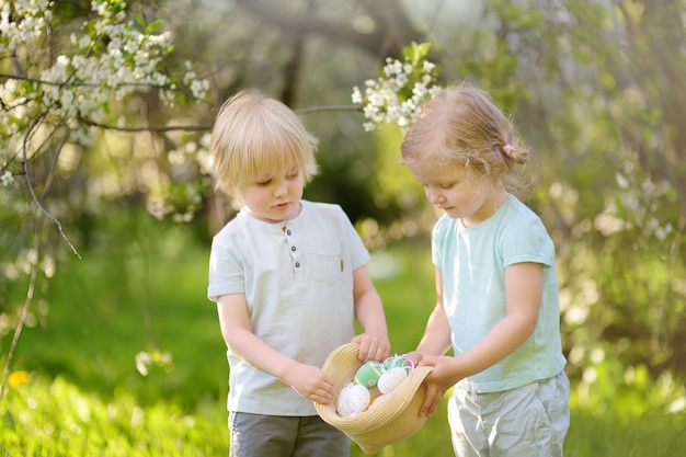 De charmants petits enfants chassent les œufs peints dans le parc du printemps le jour de Pâques.