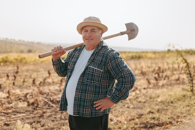 Charme rural un fermier caucasien regardant la caméra se promène à travers la campagne à la pelle sur son