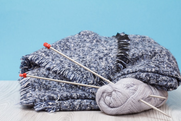 Écharpe et écheveaux de fil avec des aiguilles à tricoter en métal sur des planches grises et un fond bleu. Notion de tricot.