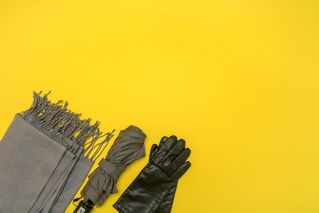 Écharpe grise et parapluie gris avec des gants sur fond jaune avec espace de copie