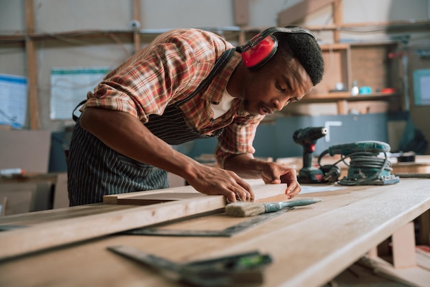 Photo un charpentier africain mesure le bois et le bois à l'aide d'outils électriques