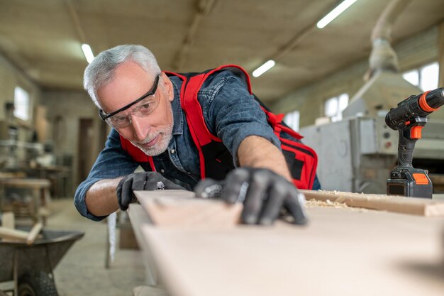 Charpentier au travail. Charpentier en galsses de protection travaillant avec du bois et ayant l'air concentré