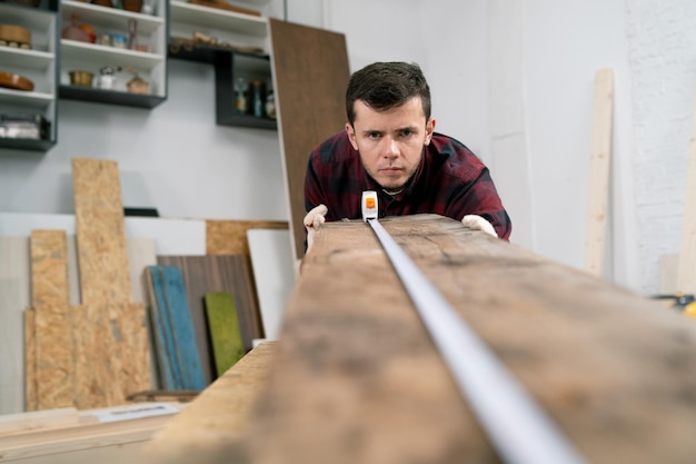 Charpentier au travail l'homme mesure et marque la planche de bois avec une règle et un crayon en métal