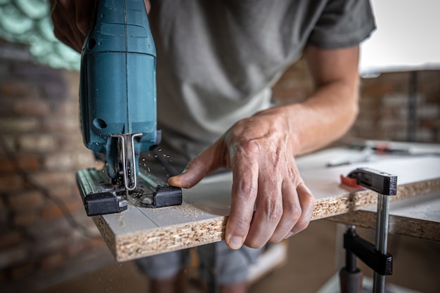 Un charpentier coupe un bois avec une scie sauteuse électrique, travaillant avec un arbre.