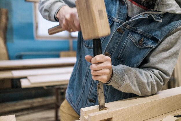 Le charpentier fait un trou dans le détail des meubles en bois avec un marteau et un ciseau