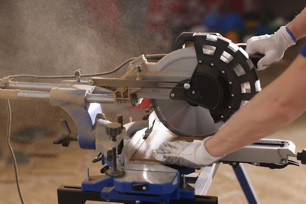 Charpentier en gants de coton coupe des planches de bois avec une machine à scier dans l'atelier le travailleur utilise le disque