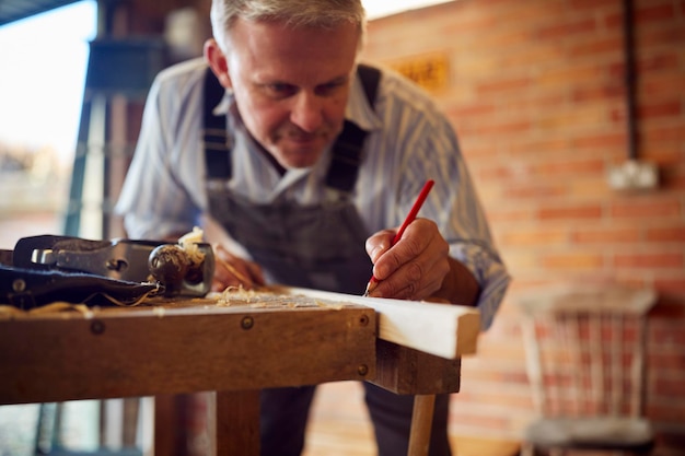 Photo charpentier mâle mature dans l'atelier de garage marquage du bois avec un crayon