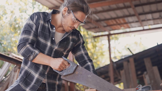 Charpentier masculin utilisant une scie à main pour couper une planche de bois à l'atelier de menuiserie