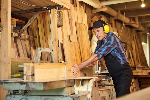 Charpentier principal en uniforme travaille sur une machine à bois à la fabrication de menuiserie