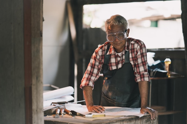 Photo charpentier senior utilisant un crayon et regardant le plan du projet travaillant sur des machines à bois dans un atelier de menuiserie homme travaille dans un atelier de menuiserie