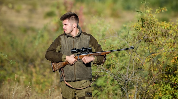 La chasse est un passe-temps masculin brutal. Saisons de chasse et de piégeage. Le chasseur sérieux barbu passe la chasse de loisirs. Fond de nature de garde-chasse non rasé brutal de l'homme. Permis de chasse. Le chasseur tient le fusil.